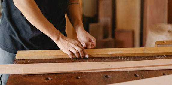 Person measuring a wooden plank with a ruler in a woodworking workshop.