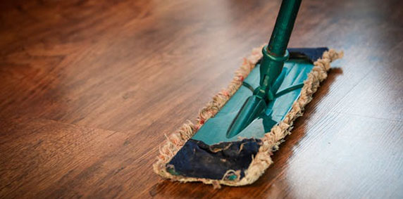 A green mop head cleaning a wooden floor, showing a portion of the mop and the smooth, polished wood surface.