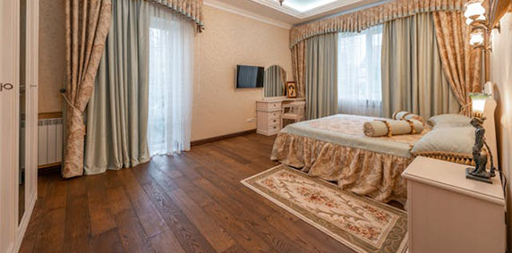 A cozy bedroom featuring a bed, a television on the wall, and a dresser against the side.